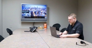 Conference room with TV on wall and employee sitting in front of a laptop