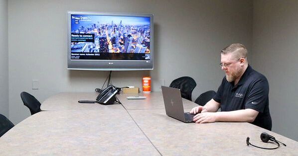 Conference room with TV on wall and employee sitting in front of a laptop