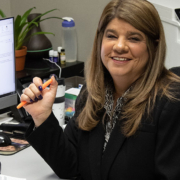 Traci Leffner sitting at her desk holding an orange pen