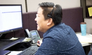 Help Desk employee with headset in front of computer in Sovran office, smiling while talking to client.