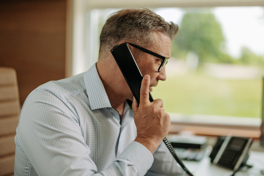 IT services professional at office desk on phone call with large window behind them.