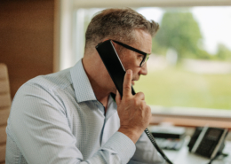 IT services professional at office desk on phone call with large window behind them.