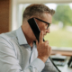 IT services professional at office desk on phone call with large window behind them.