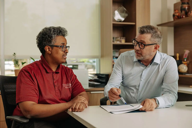 Two men at a desk reviewing options on a sheet of paper.