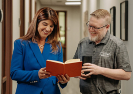 A man and a woman looking at a book in a hallway.