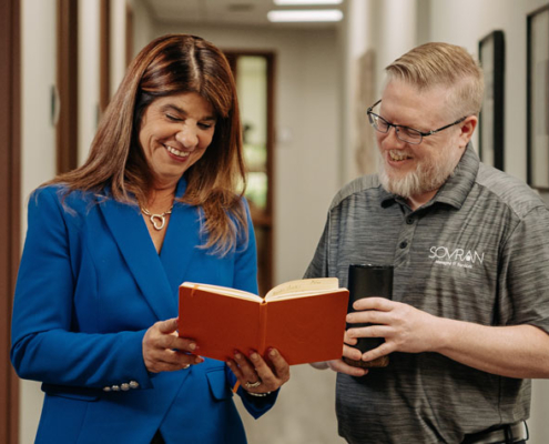 A man and a woman looking at a book in a hallway.
