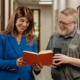 A man and a woman looking at a book in a hallway.