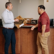 Two men are talking while one is holding a laptop package.