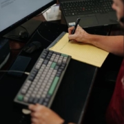 An IT support person writing on a notepad next to a computer keyboard.