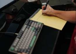 An IT support person writing on a notepad next to a computer keyboard.